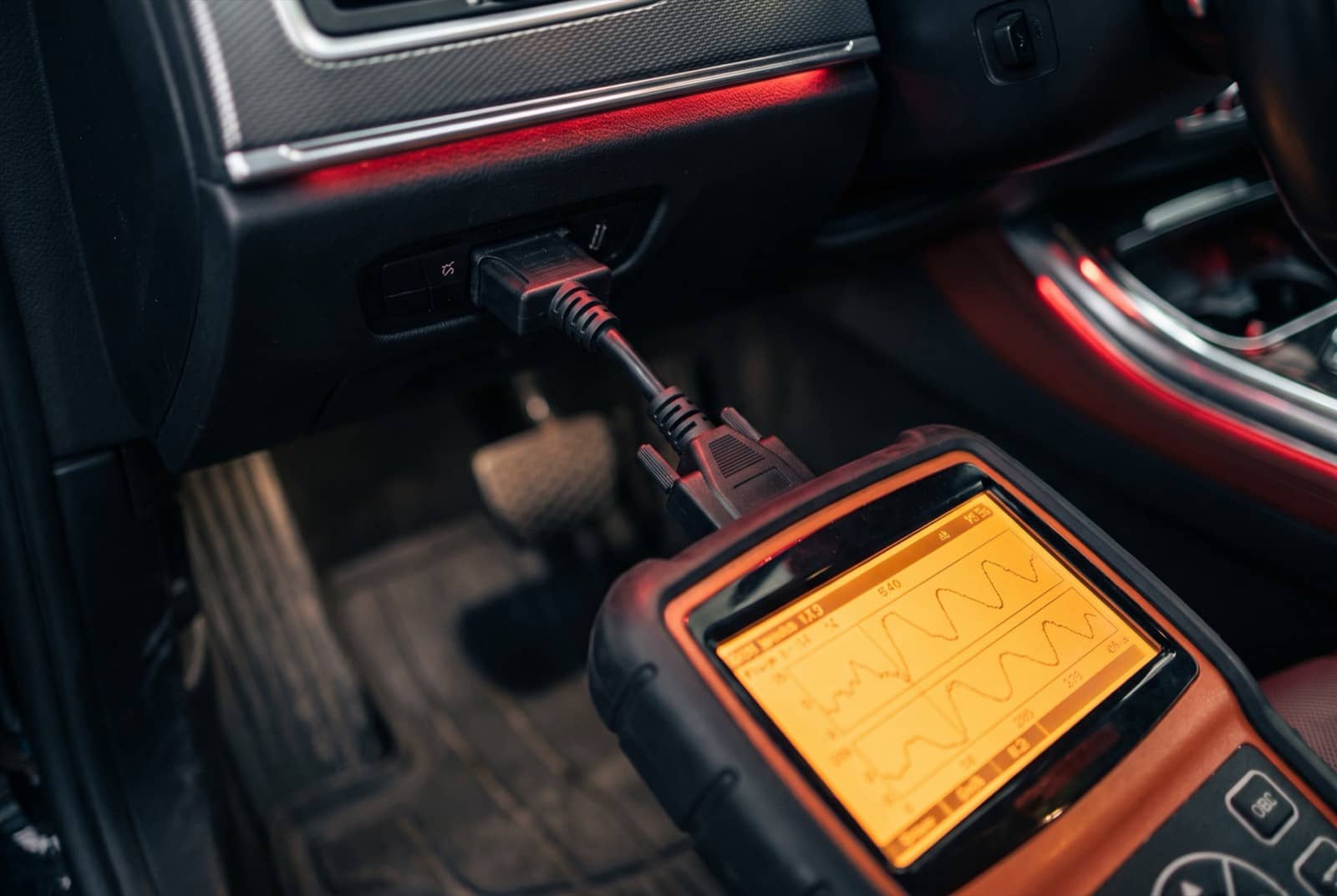 Diagnostic scan tool plugged into an OBD port under the dash, screen showing live data graphs