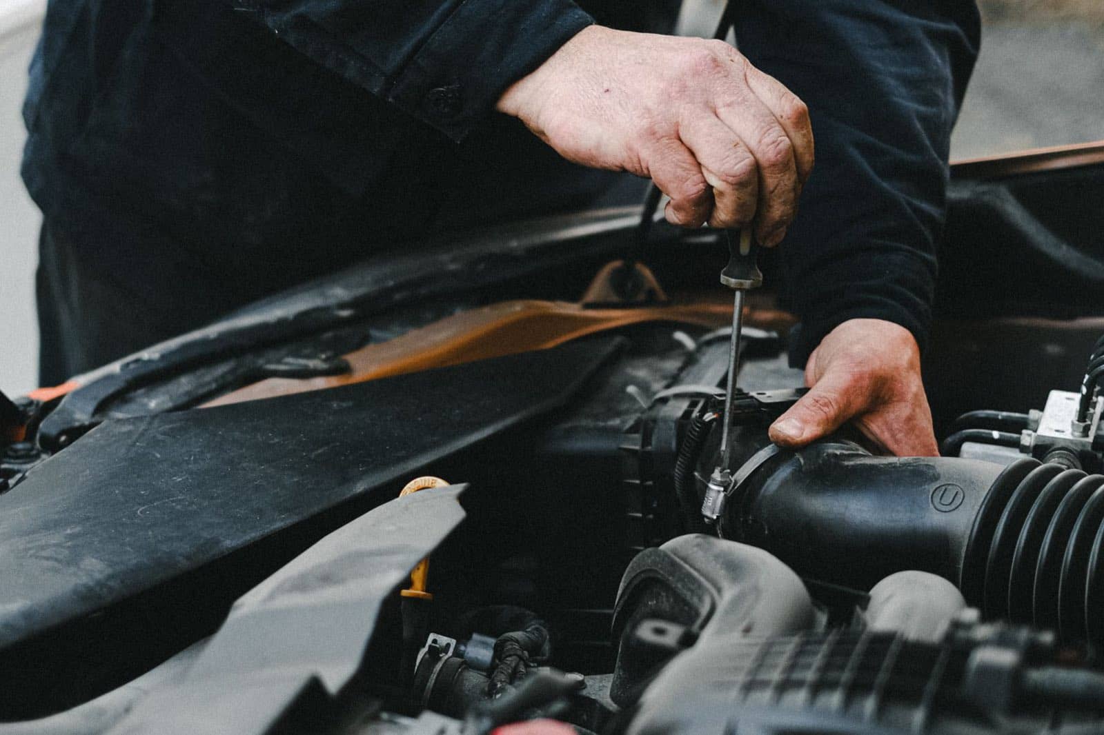 Mechanic tightening an intake hose clamp with a screwdriver under the hood