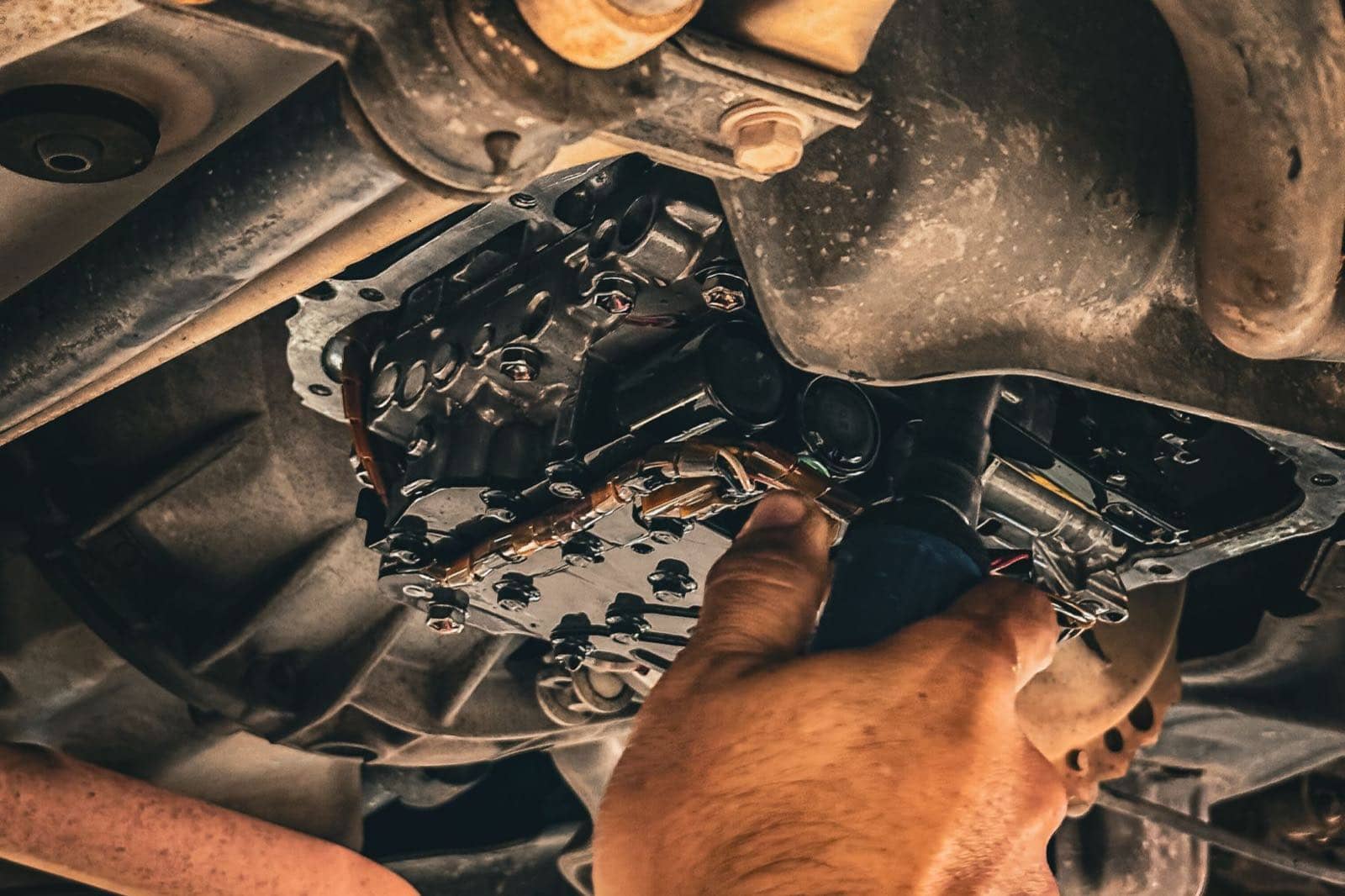 Mechanic's hand working on a transmission from underneath a raised vehicle