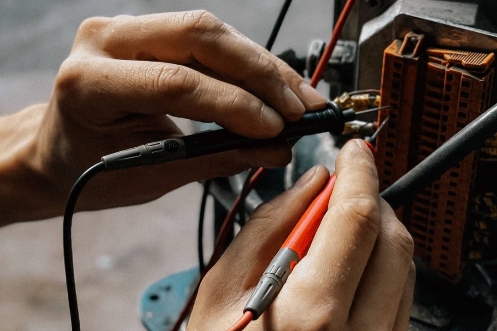 Hands holding multimeter probes against a wiring terminal block